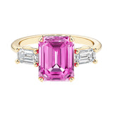 Emerald cut 3 stone engagement ring with pink gemstone and diamond accents.