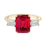 Emerald cut 3 stone engagement ring with red gemstone and diamond accents.