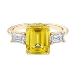 Emerald cut 3 stone engagement ring with yellow gemstone and diamond accents.