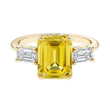Emerald cut 3 stone engagement ring with yellow gemstone and diamond accents.