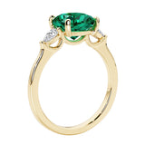Three stone cushion diamond ring in yellow gold setting with green emerald and diamonds.