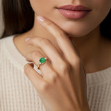 Woman wearing a cushion cut 3 stone ring with romantic styling featuring colombian emerald and diamonds.
