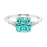 Cushion shaped engagement ring with brilliant diamonds and green gemstone.