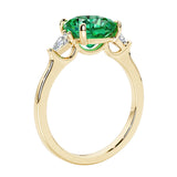 Three stone cushion diamond ring in yellow gold setting with green gemstone and diamonds.