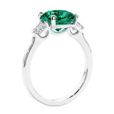 Cushion cut diamond ring as a unique engagement ring featuring three stone design with green gemstone and diamonds.