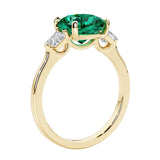 Three stone cushion diamond ring in yellow gold setting with green gemstone and diamonds.
