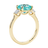 Three stone cushion diamond ring in yellow gold setting with green gemstone and diamonds.