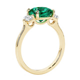 Three stone cushion diamond ring in yellow gold setting with green gemstone and diamonds.