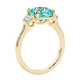 Three stone cushion diamond ring in yellow gold setting with green gemstone and diamonds.