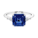 Asscher gemstone diamond ring with step-cut sparkle in a three stone setting featuring blue sapphire center.