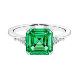 Asscher gemstone diamond ring with step-cut sparkle in a three stone setting featuring colombian emerald center.