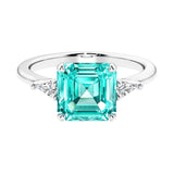 Asscher gemstone diamond ring with step-cut sparkle in a three stone setting featuring paraiba tourmaline center.