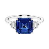 Asscher gemstone diamond ring with step-cut sparkle in a three stone setting featuring blue sapphire center.