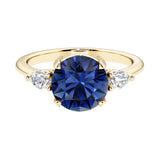 Three stone round engagement ring with a brilliant round blue sapphire center diamond and two round side stones.