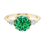 A 14k yellow gold three stone round engagement ring with a brilliant round colombian emerald center diamond and two round side stones.