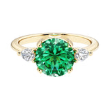 A 14k yellow gold three stone round engagement ring with a brilliant round colombian emerald center diamond and two round side stones.