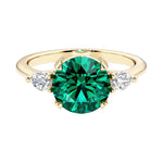 A 14k yellow gold three stone round engagement ring with a brilliant round emerald center diamond and two round side stones.