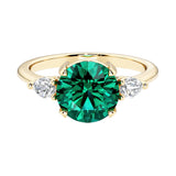 A 14k yellow gold three stone round engagement ring with a brilliant round emerald center diamond and two round side stones.