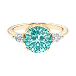 A 14k yellow gold three stone round engagement ring with a brilliant round paraiba green tourmaline center diamond and two round side stones.