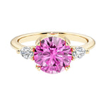 A 14k yellow gold three stone round engagement ring with a brilliant round pink sapphire center diamond and two round side stones.
