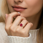 Woman wearing a 14k gold three stone round engagement ring with red ruby and dazzling diamonds.