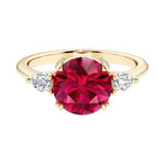 A 14k yellow gold three stone round engagement ring with a brilliant round red ruby center diamond and two round side stones.