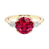 A 14k yellow gold three stone round engagement ring with a brilliant round red ruby center diamond and two round side stones.