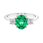 Three stone oval cut emerald gemstone and diamond ring in classic design.