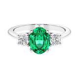 Three stone oval cut emerald gemstone and diamond ring in classic design.