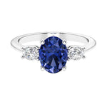 Three stone oval cut diamond ring in classic design featuring blue sapphire center.
