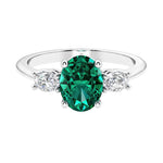 Three stone oval cut diamond ring in classic design featuring emerald center.