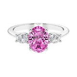 Three stone oval cut diamond ring in classic design featuring pink sapphire center.