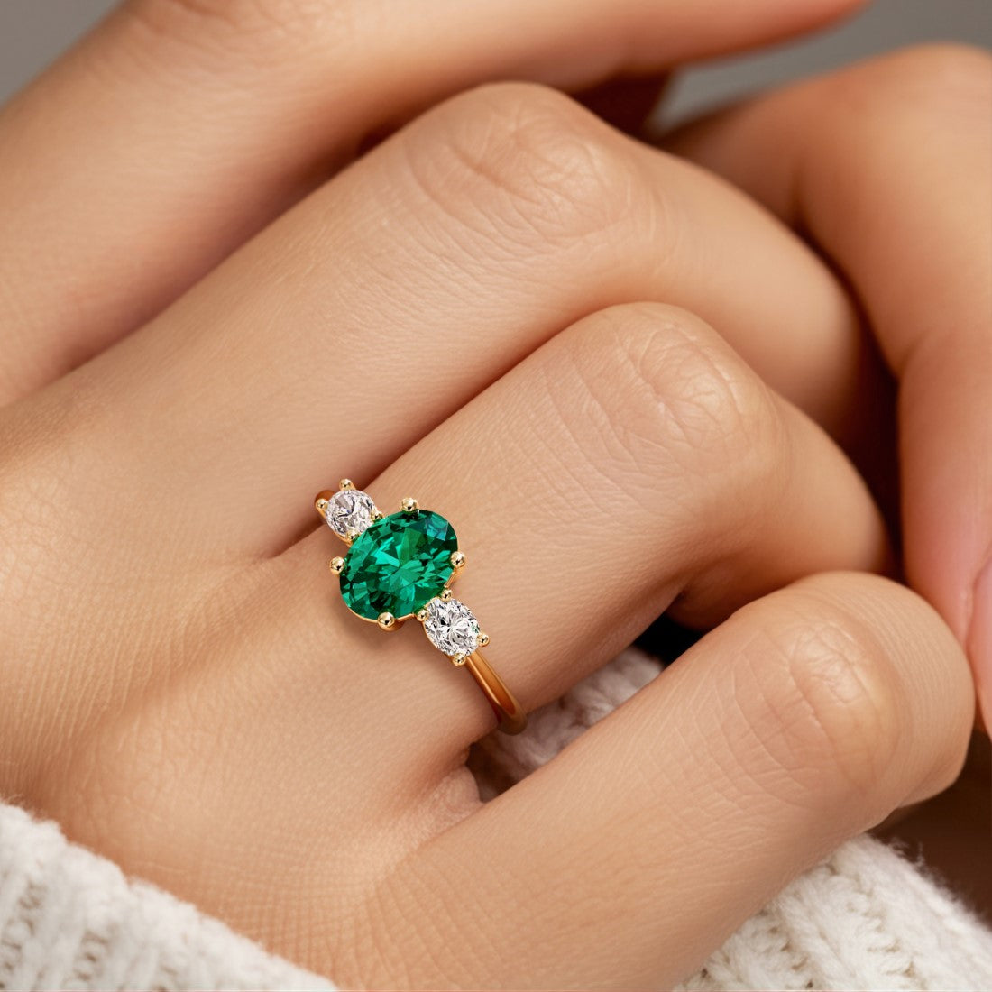 Hand adorned with oval 3 stone diamond ring in yellow gold featuring real emerald.
