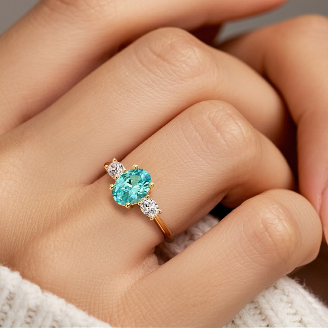 Hand adorned with oval 3 stone diamond ring in yellow gold featuring paraiba green tourmaline.