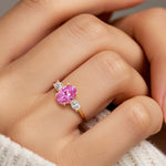 Hand adorned with oval 3 stone diamond ring in yellow gold featuring pink sapphire.