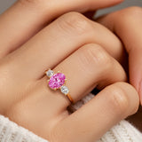 Hand adorned with oval 3 stone diamond ring in yellow gold featuring pink sapphire.