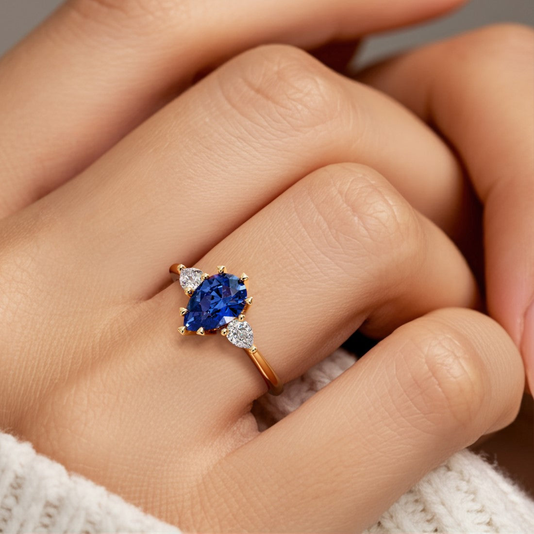 Woman wearing pear shaped three stone engagement ring with romantic flair.