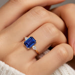 Woman wearing emerald cut three stone engagement ring with bold lines.