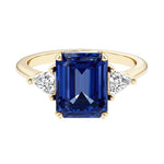 Emerald cut 3 stone engagement ring with blue gemstone and diamond accents.