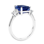 3 stone emerald cut diamond ring in modern gold setting with blue gemstone center.