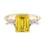 Emerald cut 3 stone engagement ring with yellow gemstone and diamond accents.