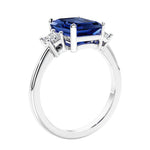 3 stone emerald cut diamond ring in modern gold setting with blue gemstone center.