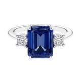 Three stone emerald cut engagement ring for timeless elegance featuring blue gemstone and diamonds.
