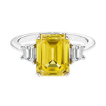 Three stone emerald cut engagement ring for timeless elegance featuring yellow gemstone and diamonds.