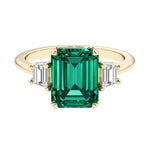 Emerald cut 3 stone engagement ring with green gemstone and diamond accents.