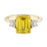 Emerald cut 3 stone engagement ring with yellow gemstone and diamond accents.