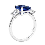 3 stone emerald cut diamond ring in modern gold setting with blue gemstone center.