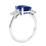 3 stone emerald cut diamond ring in modern gold setting with blue gemstone center.
