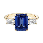 Emerald cut 3 stone engagement ring with blue gemstone and diamond accents.