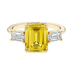 Emerald cut 3 stone engagement ring with yellow gemstone and diamond accents.